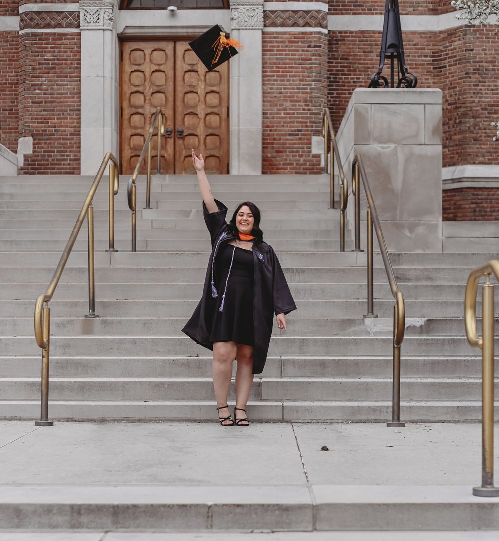Graduate in black cap and gown celebrating on historic building steps.