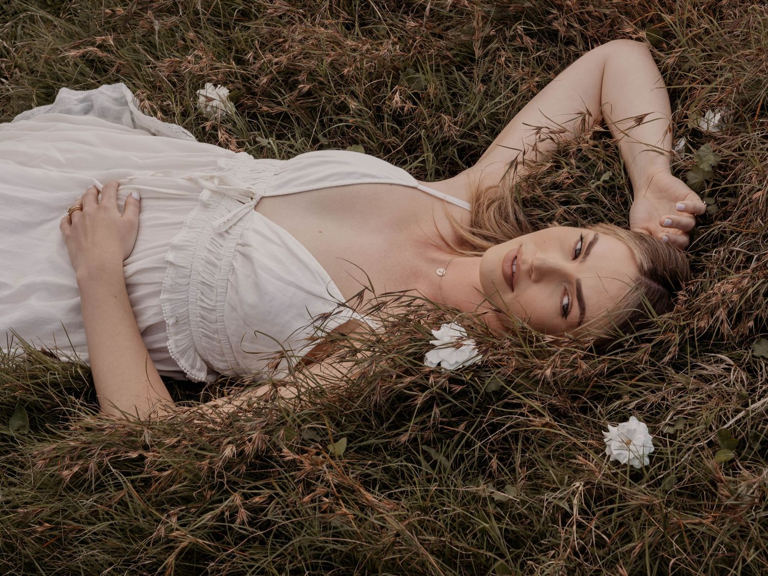 Woman in white dress lying in field with wildflowers at dusk.