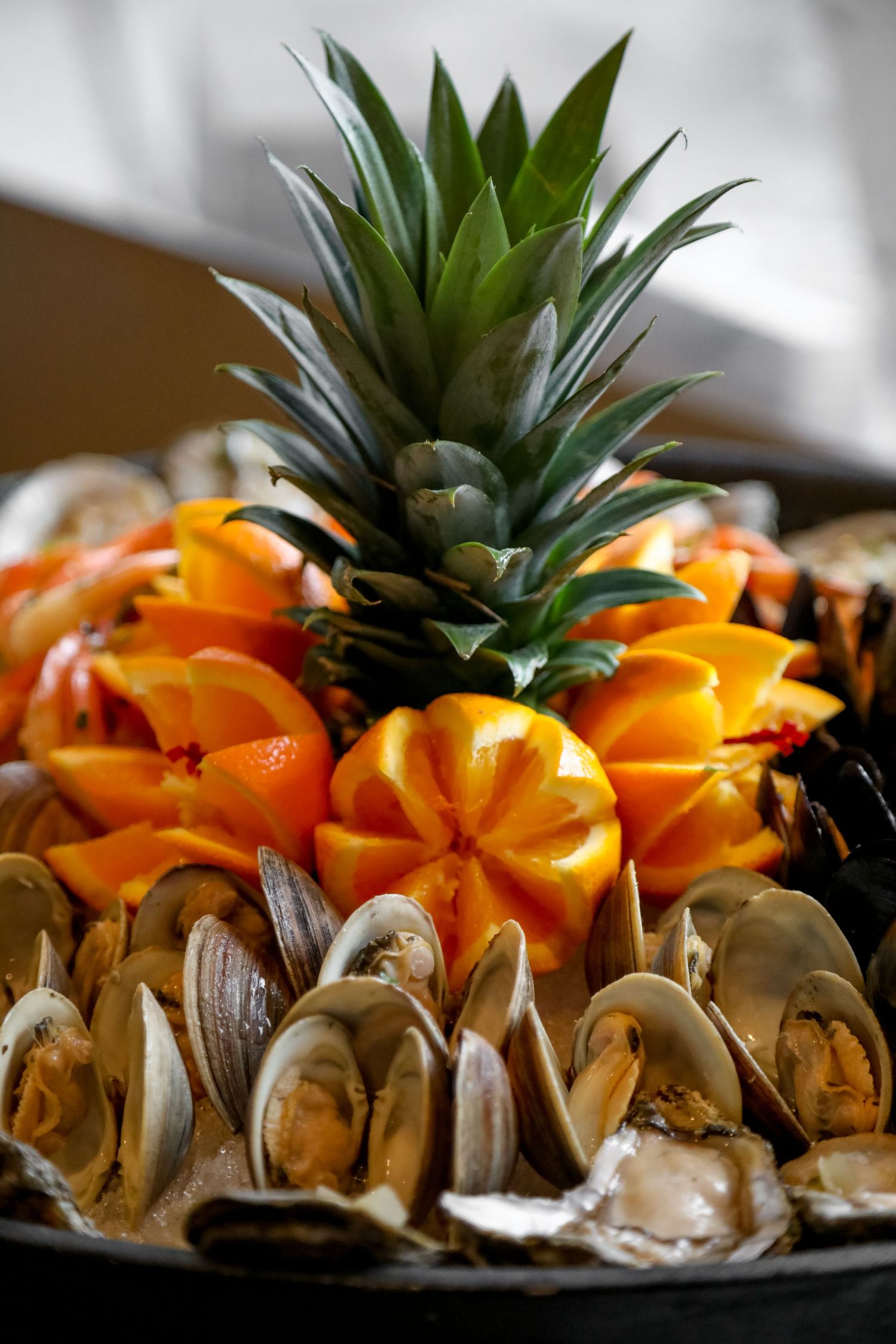 Close up of fresh seafood platter with steamed clams and oranges garnished with a whole pineapple on top.