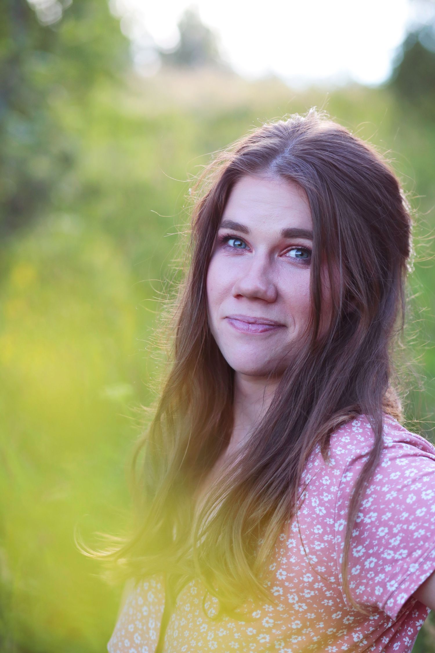 An outdoor portrait of a person with long hair wearing a floral dress against a blurred natural background.