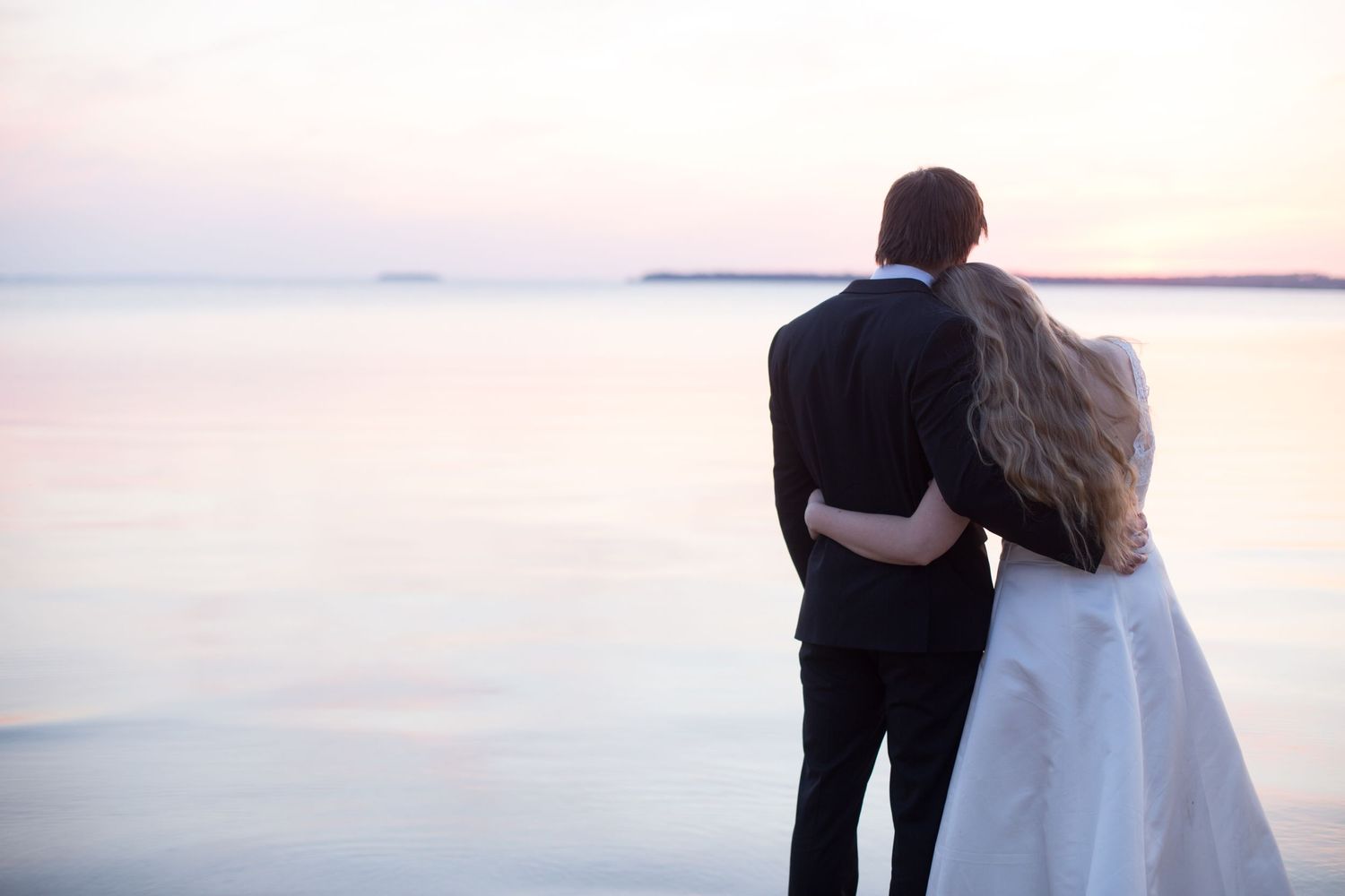 Romantic silhouette of couple embracing while watching sunset over water.