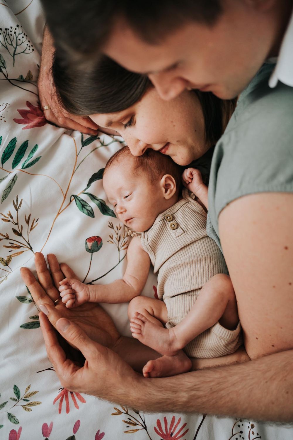 Noworodek, mama i tata leżą na łóżku i się przytulają - naturalna sesja Kraków