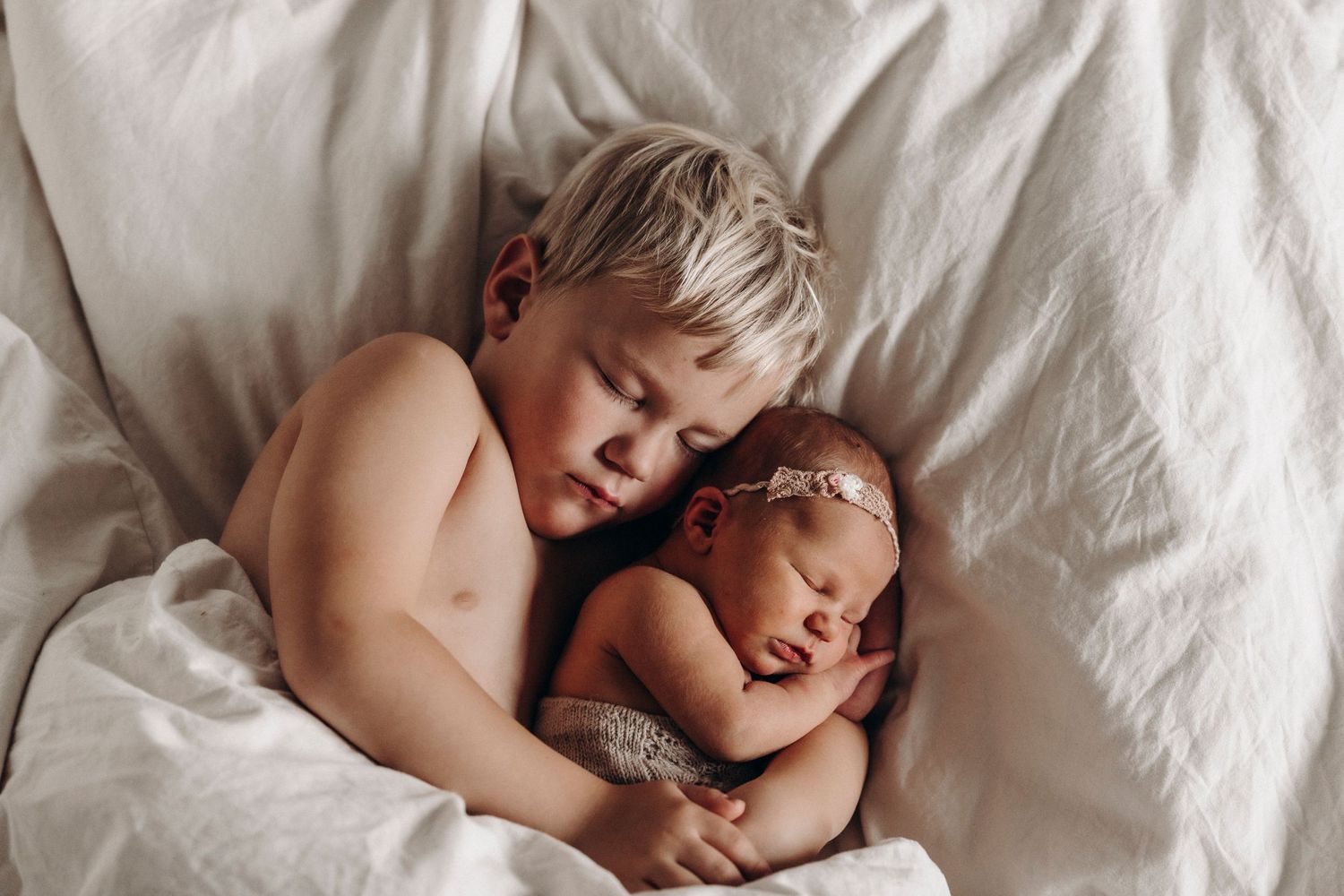 Two toddlers sleeping sweetly together on white bedding.
