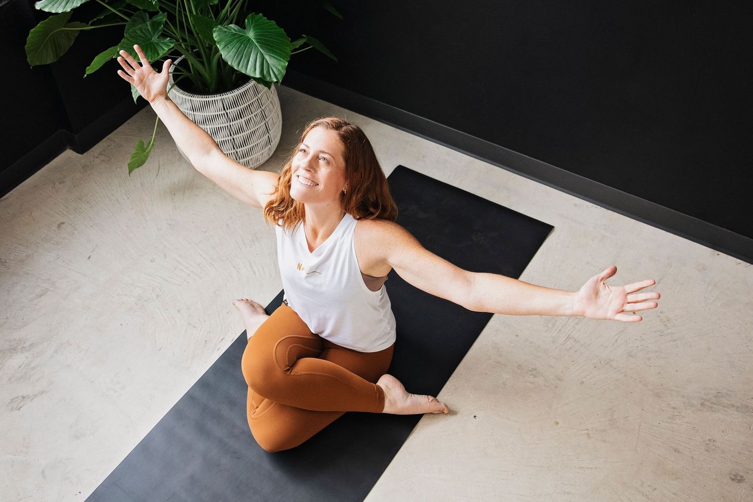 Person performing expressive yoga pose on light floor with dramatic lighting.
