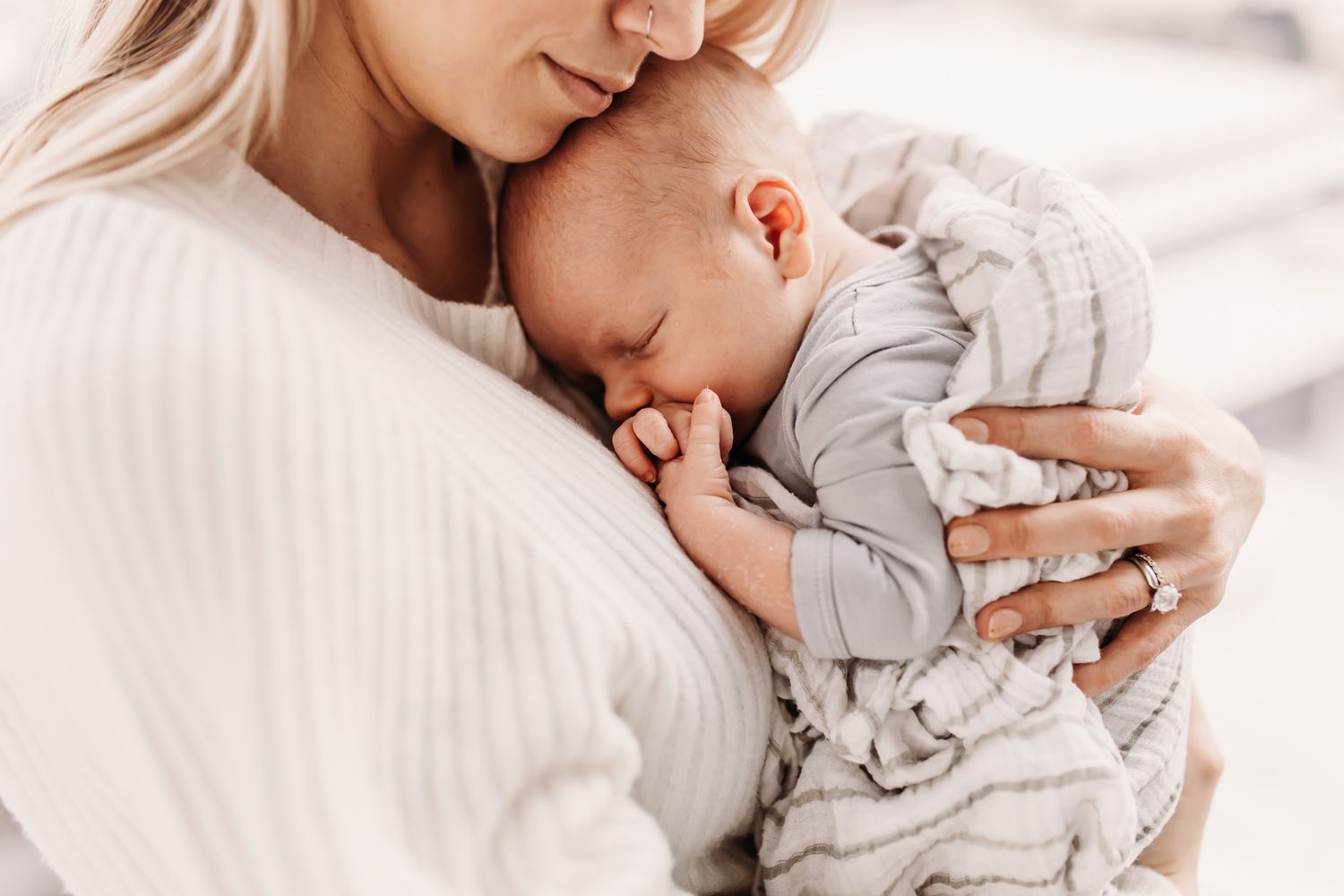 Tender moment captured as parent in white cradles sleeping baby in gray outfit.