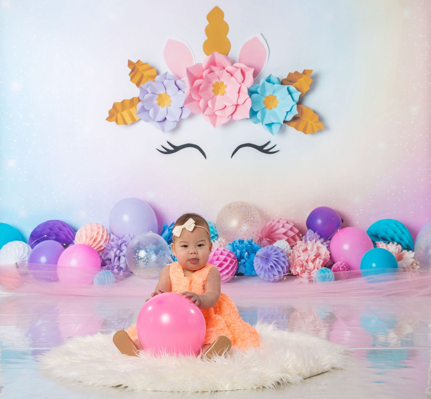 Unicorn themed cake smash photo with pastel balloons and floral wall decorations.