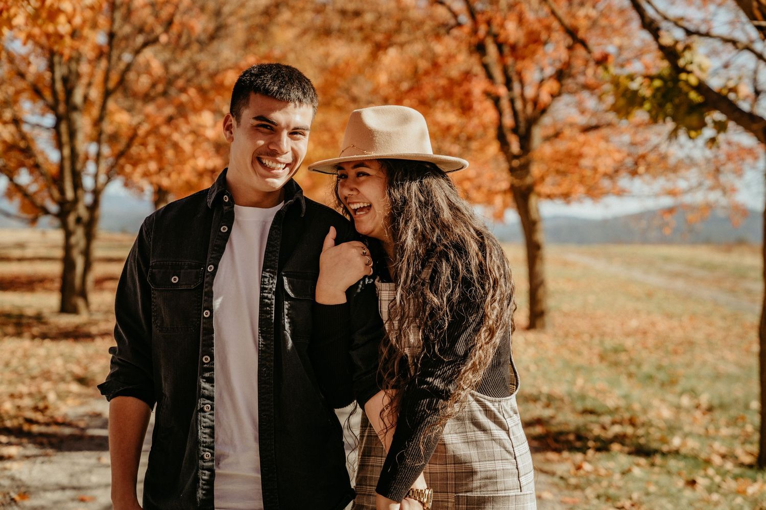 Couple laughing together in autumn setting with orange foliage.