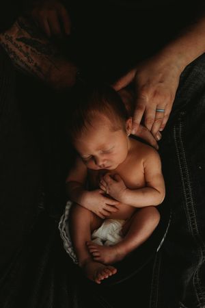 Newborn nestled into a motorcycle helmet, tucked safely beneath parents hands.