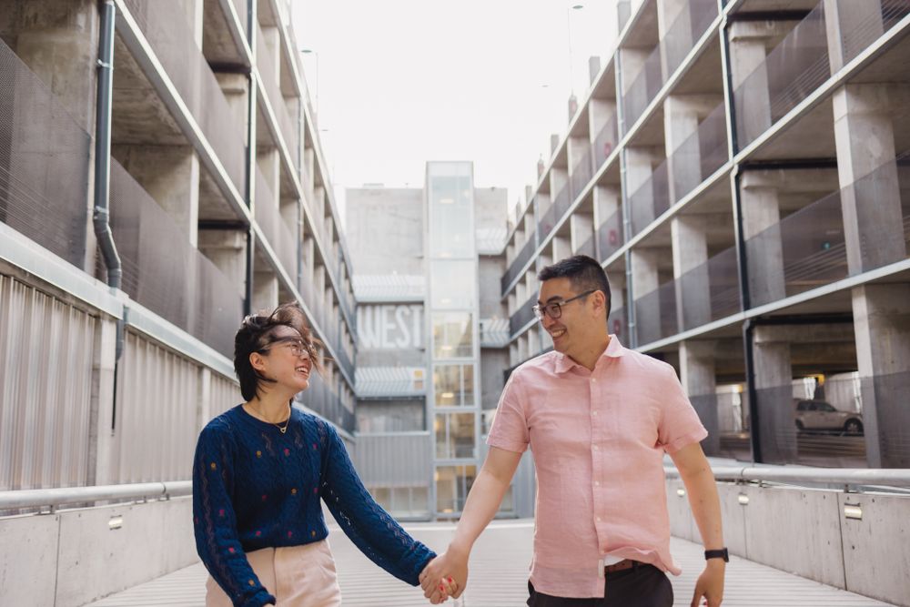 Couple walking and laughing together along an urban walkway with modern architecture.