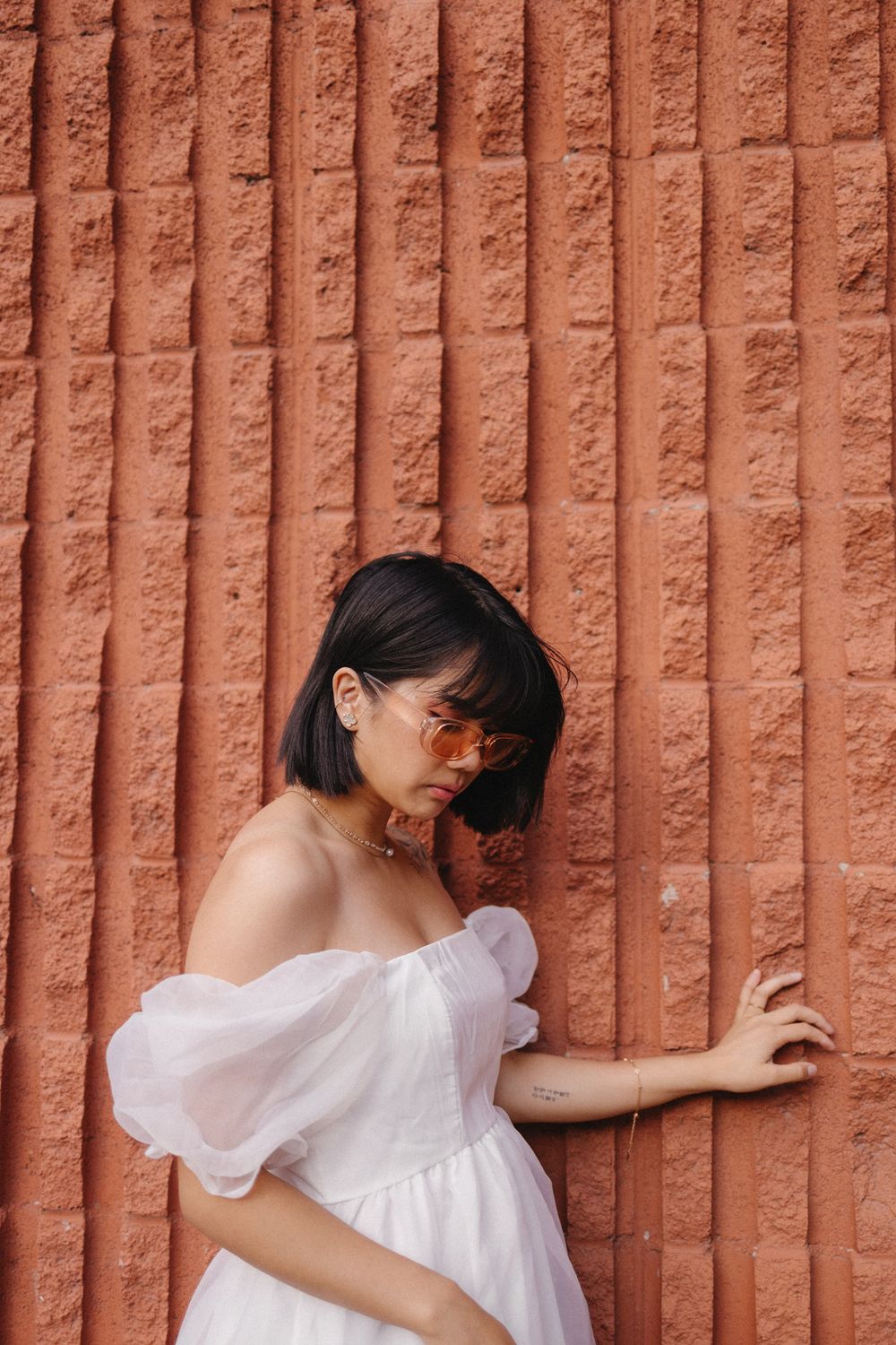 A person in a white dress poses against a textured terracotta wall in different artistic positions.