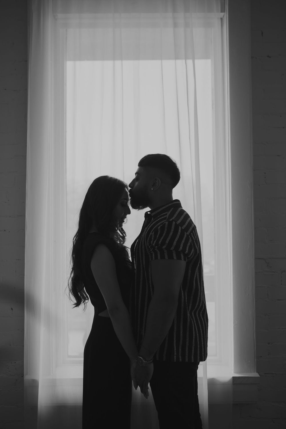 Artistic black and white silhouettes of a couple in romantic poses against a bright window background.