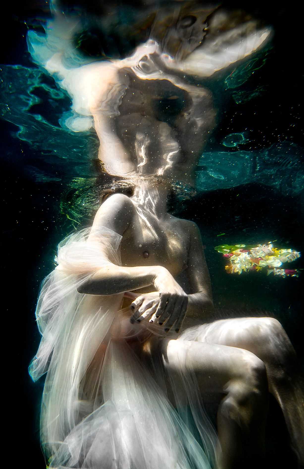 Underwater photography of flowing white dress creating ethereal movement in turquoise waters.