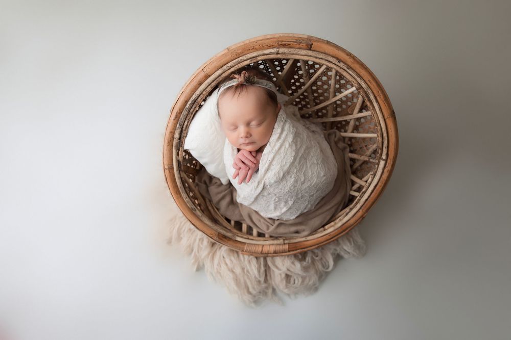 Sleeping newborn wrapped in white blanket nestled in round woven basket.