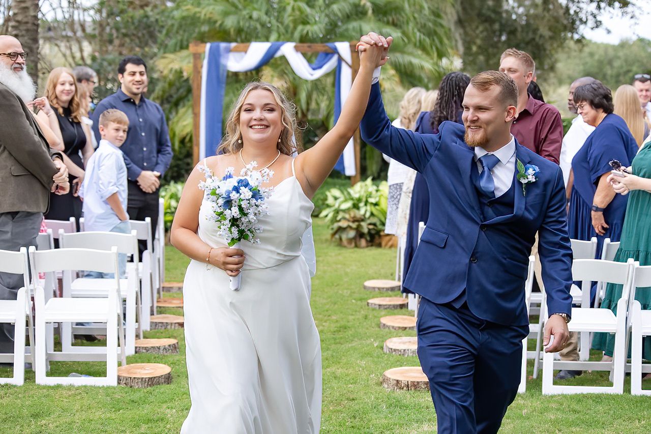 Wedding celebration outdoors with guests seated in white chairs on a grassy lawn.