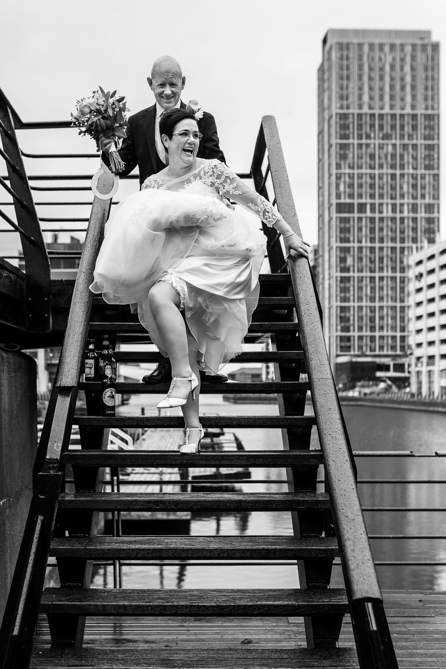 Bride lifts up her wedding dress to show off her garter as she walks down a metal staircase on the Liverpool waterfront.