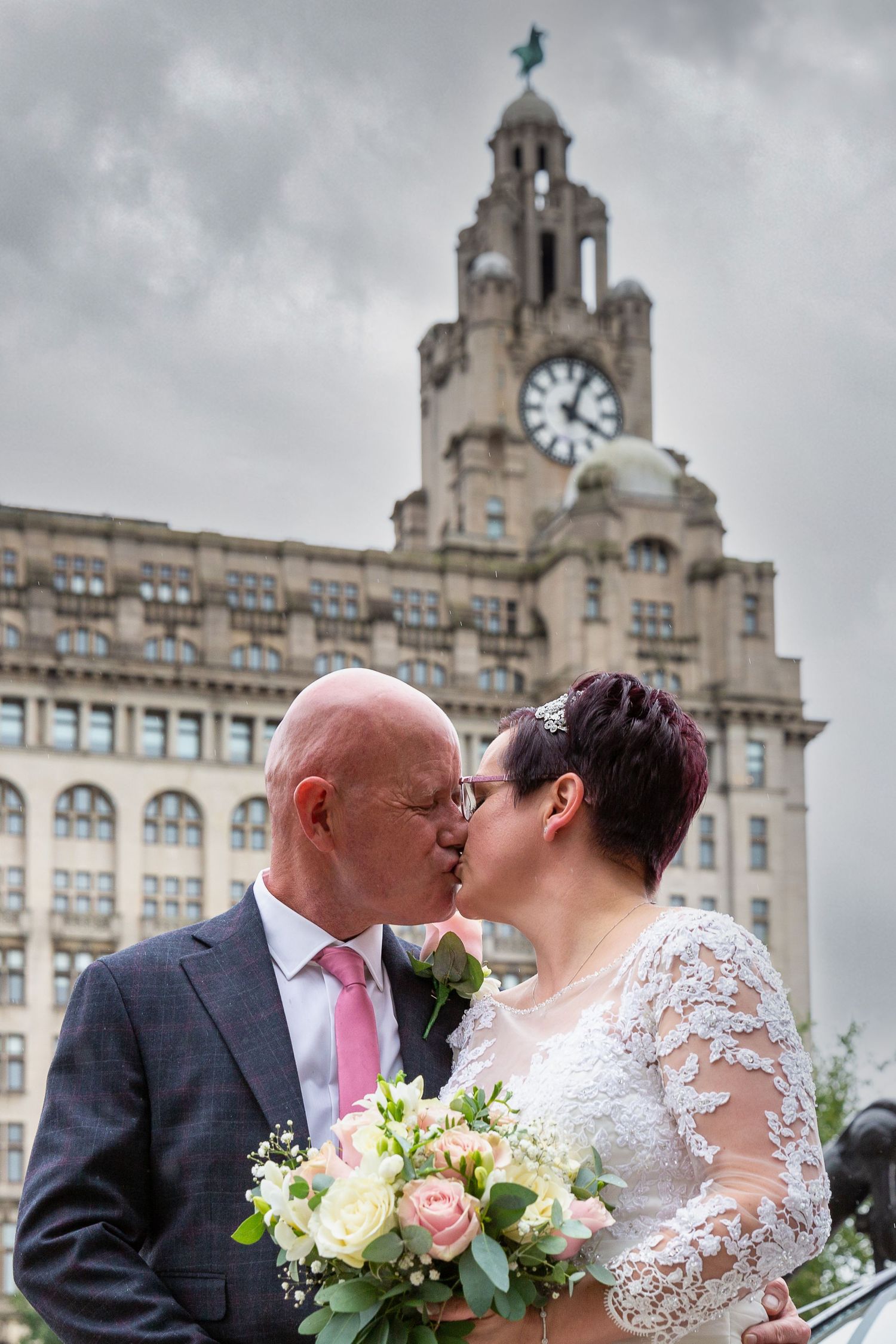 Bride and groom share a kiss standing in front of the liver building on the Liverpool waterfront