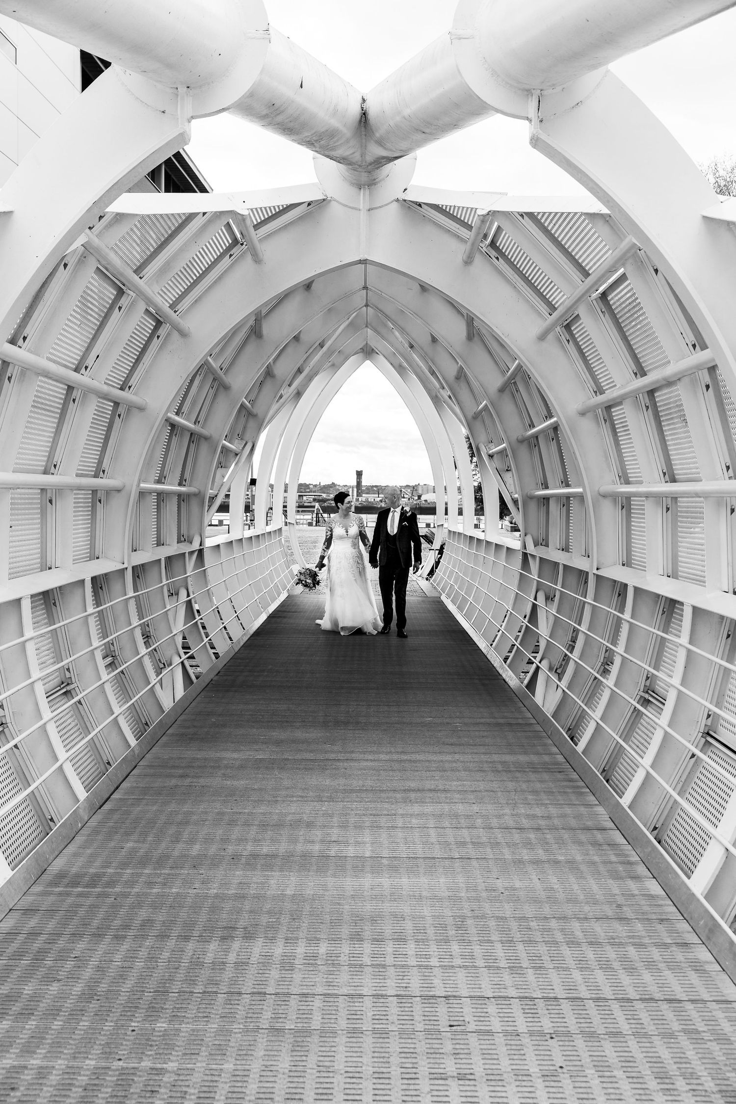 Bride and groom walk along the metal bridge at Princes Dock On the Liverpool waterfront