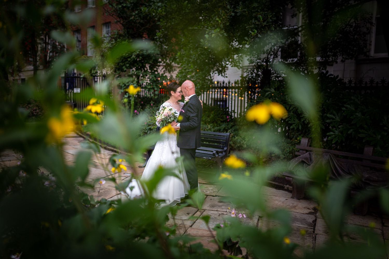 Bride and groom kissing in Saint Nicholas Gardens Liverpool, photograph shot through a bush framing them