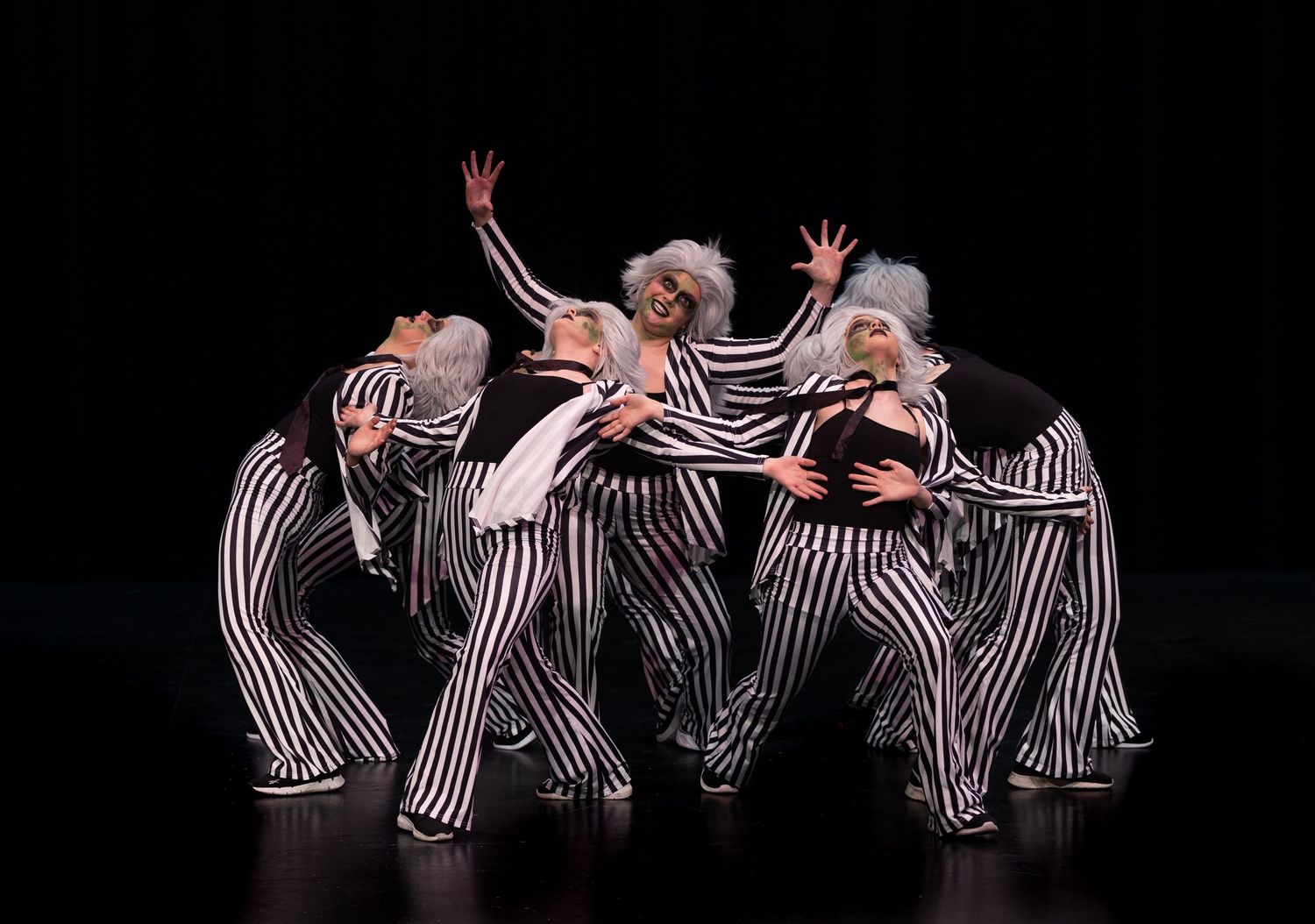 Dancers perform in striped costumes against black background in synchronized formation.