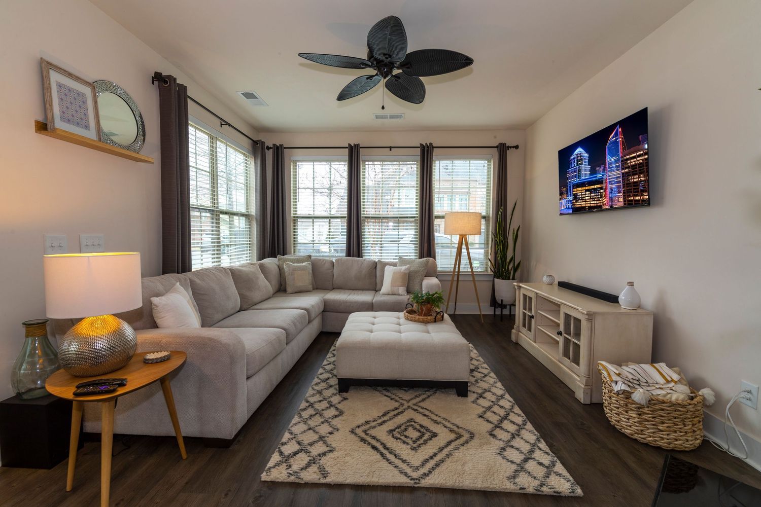 Modern bedroom interior with geometric rug, ceiling fan, and large windows providing natural light.
