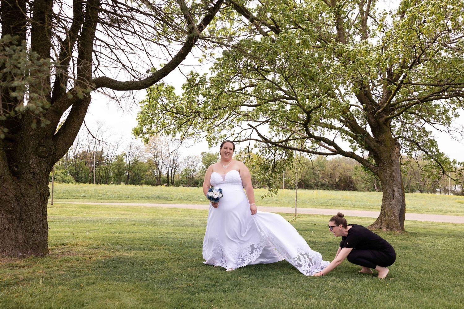 A wedding dress billows in the breeze as someone adjusts it in an outdoor garden setting.
