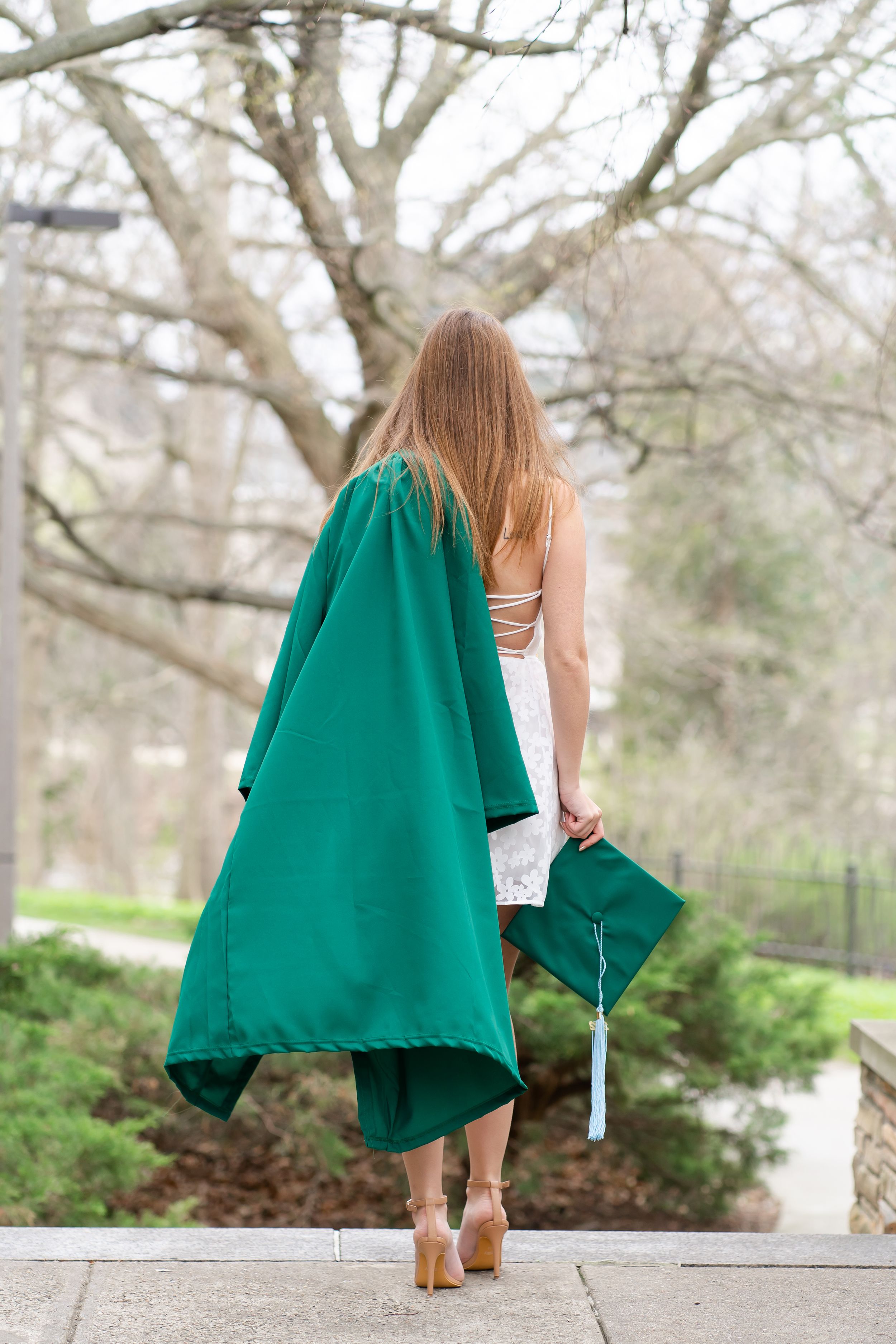 Graduate walks away, gown over shoulder, cap in hand