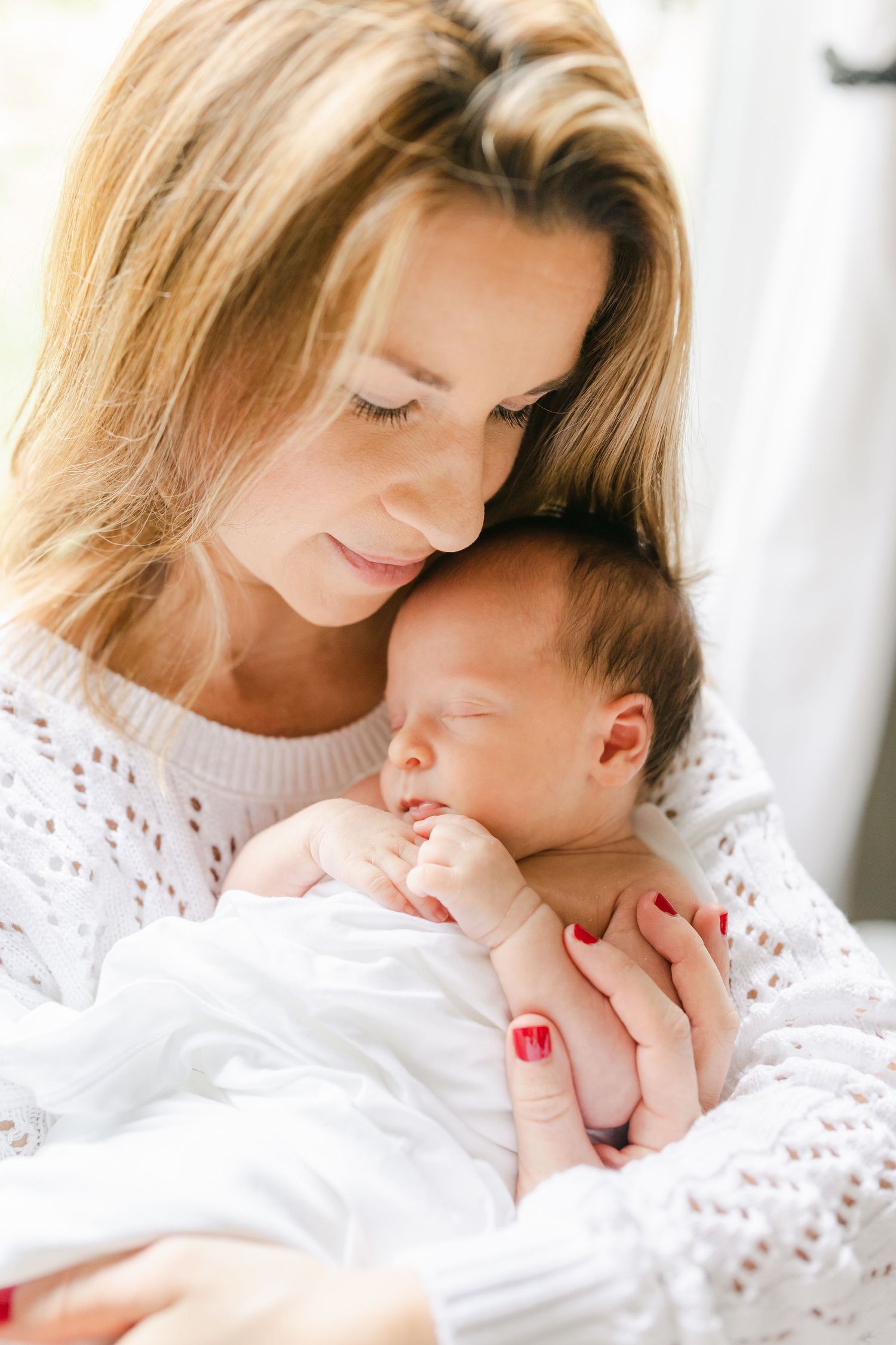 Mother holding newborn baby in nursery wearing white