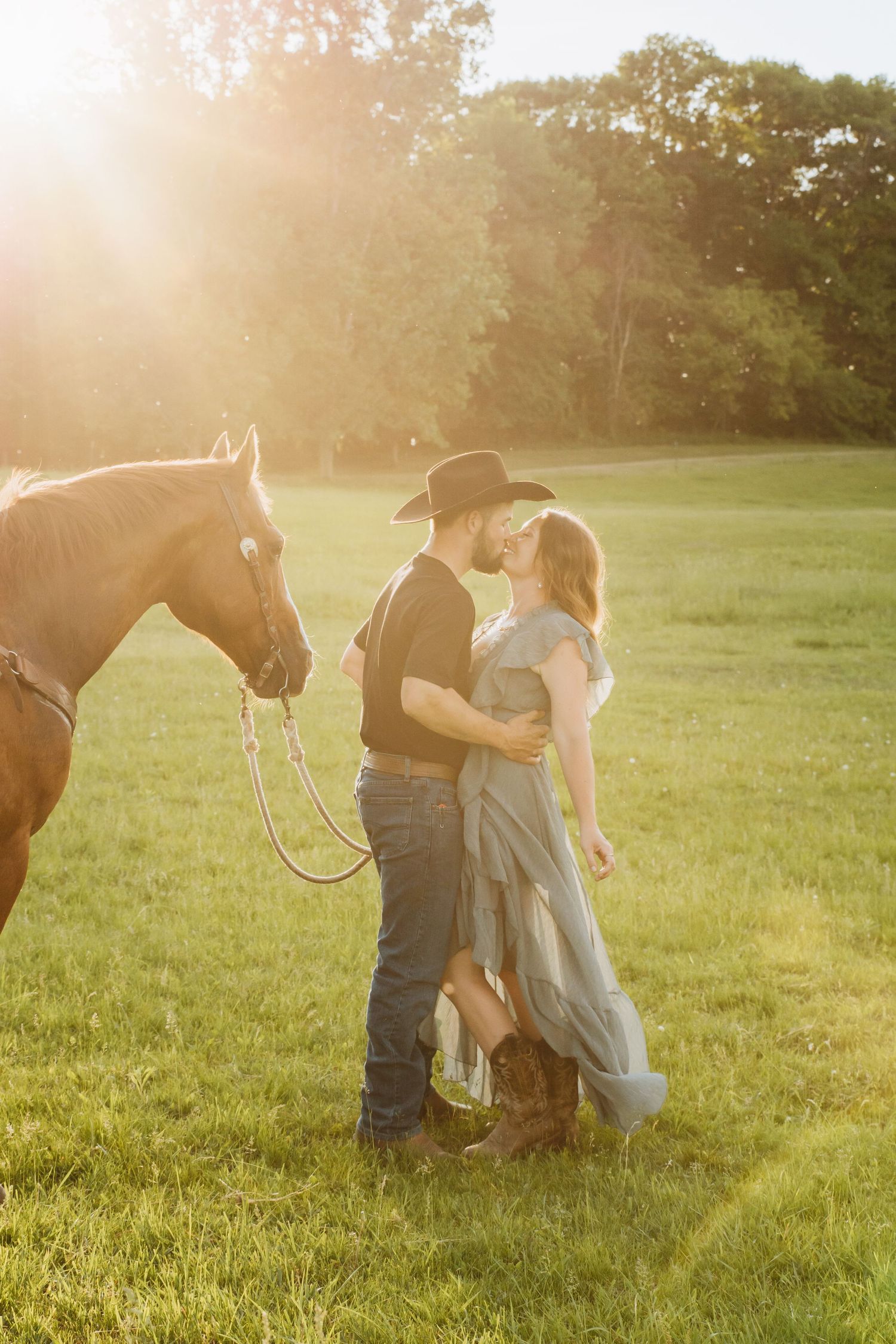 Romantic countryside photo with a horse standing beside a couple during golden hour.