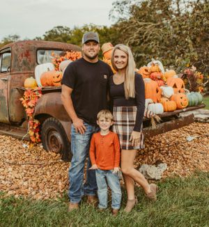 Family poses by vintage truck loaded with orange pumpkins during autumn photoshoot.