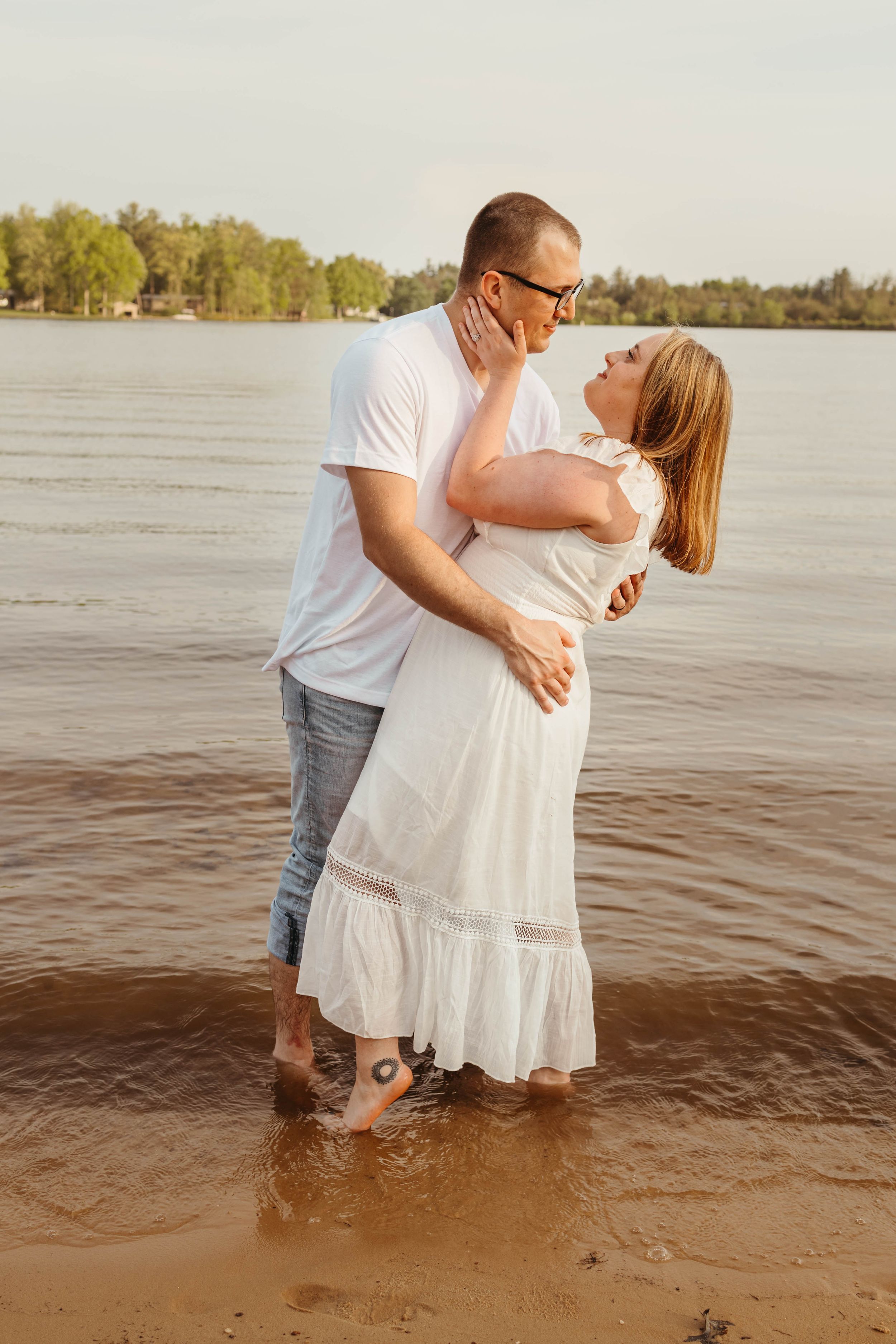 Romantic couple embracing in shallow water at sunset by the lake.
