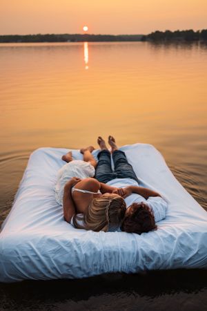 Person lying on floating mattress watching sunset over peaceful lake.
