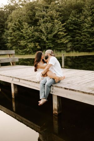 A couple sharing a romantic moment on a wooden dock overlooking a peaceful lake.
