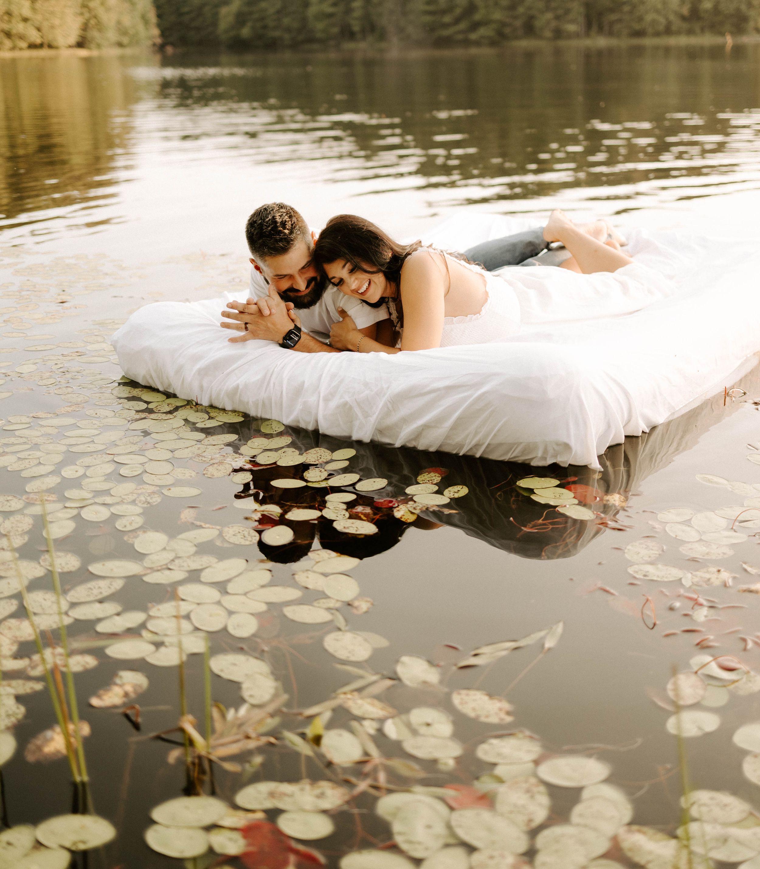 A couple lying on a floating mattress among lily pads in a peaceful lake.