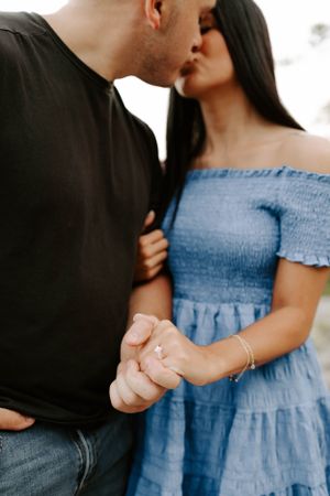 Couple holding hands with engagement ring visible, wearing contrasting black shirt and blue dress.