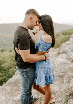 Couple embracing on mountain cliff edge with scenic valley view in background.