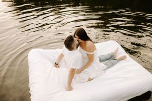 Two people sharing an intimate moment on a white floating mattress in calm waters.