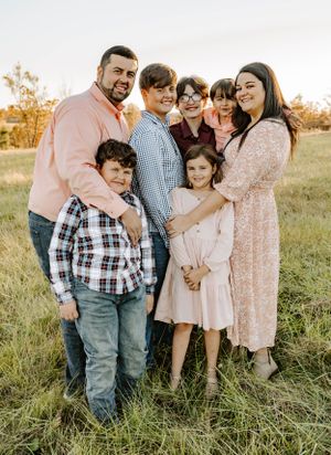 Family group portrait in coordinated pastel and plaid outfits at sunset in a grassy field.
