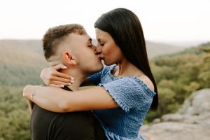 Romantic couple sharing intimate kiss against mountain landscape backdrop at sunset.