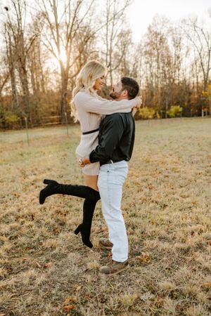 Couple sharing playful moment in field with autumn sunset behind them.