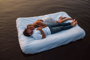 Couple relaxing on floating mattress in lake during sunset.
