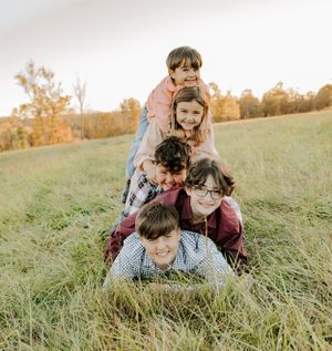 Playful stack of children lying in tall grass during a family photo session.
