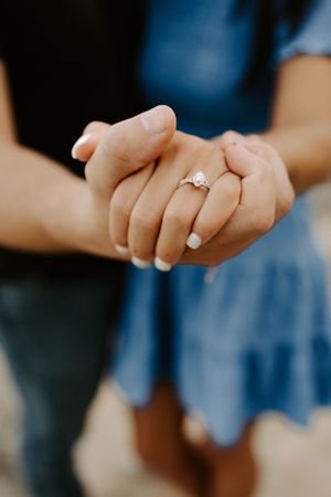 Close-up of hands holding engagement ring with sparkling diamond against blue dress.