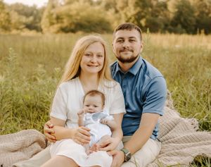 A family sitting together on a blanket in a sunlit meadow with their baby.