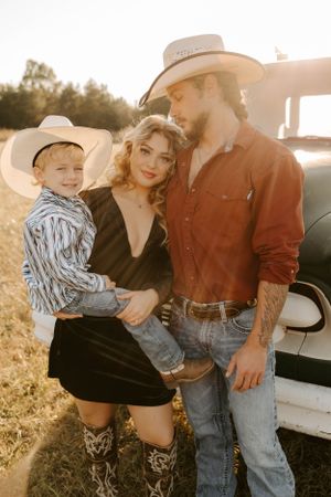 A family poses together in western attire next to a vintage pickup truck at sunset.