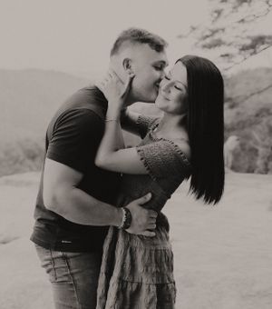 Black and white portrait of couple sharing romantic moment against mountain landscape.