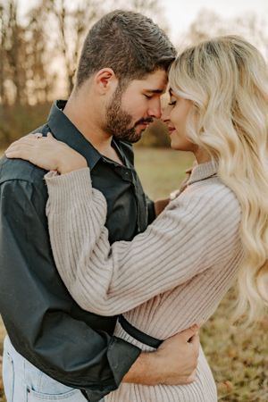 A romantic moment between a couple embracing outdoors in autumn wearing cozy sweaters.