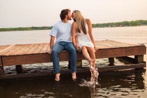 Couple sitting on wooden dock splashing feet in water at sunset.