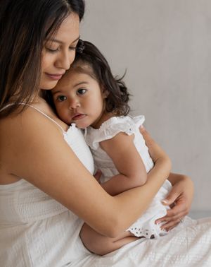 Mother and daughter in white outfits share loving embraces during an indoor photoshoot.
