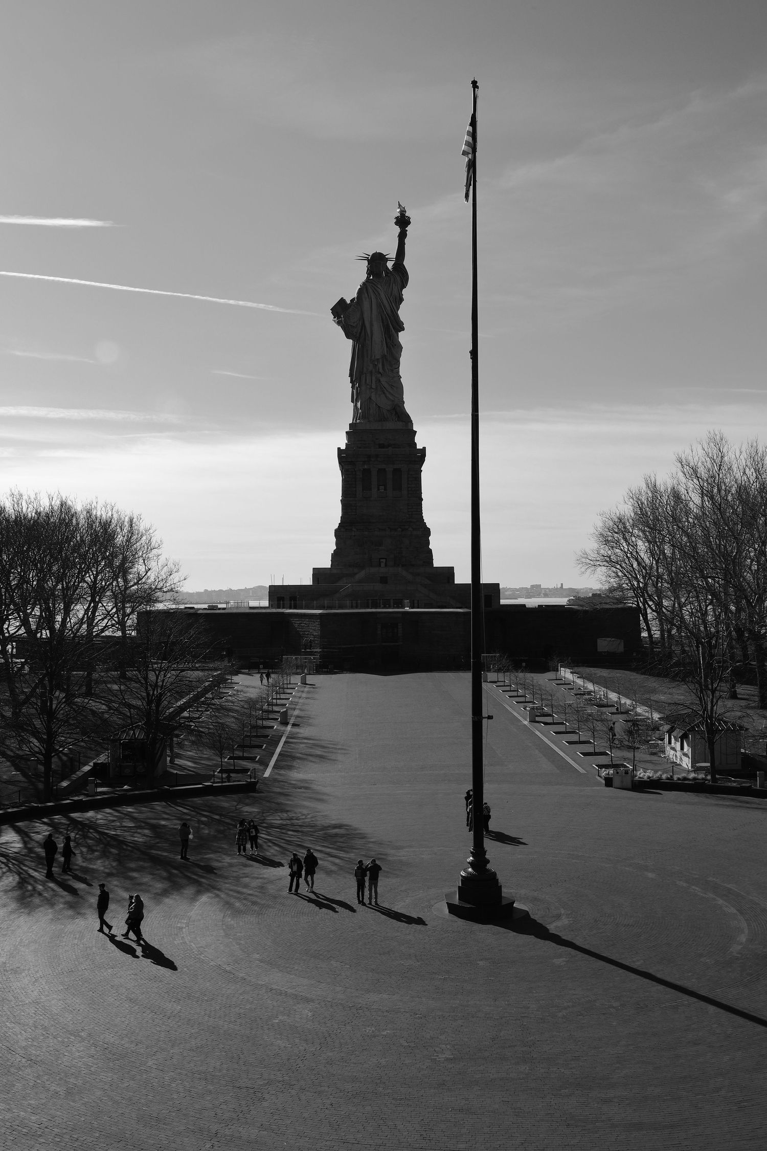 Black and white photo of the Statue of Liberty with visitors walking on the viewing platform below.