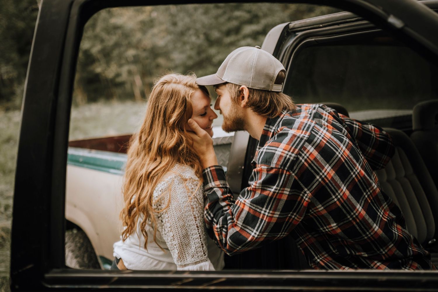 Romantic couple sharing an intimate moment in a truck with rustic outdoor backdrop.